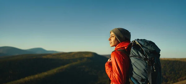 Ritratto laterale donna escursionista con zaino in piedi nella luce del tramonto tra montagne e colline — Foto Stock