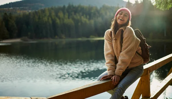 En glad latter sitter på en brygge nær en fjellsjø og nyter naturlandskapet. – stockfoto