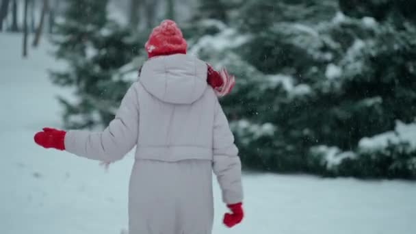Κάμερα ακολουθεί χαρούμενη ενθουσιασμένοι γυναίκα με τα πόδια και παιχνιδιάρικα τρέχει στο πάρκο στο χρόνο χιονιού. Δέντρα στέκονται στο χιόνι την παγωμένη χειμωνιάτικη μέρα — Αρχείο Βίντεο