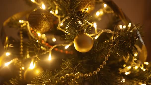 Zeitlupe Nahaufnahme goldene Zierkugel, die an Zweigen des Weihnachtsbaums im Haus hängt. Hausdekoration und Vorbereitung auf Weihnachten und Neujahr zu Hause — Stockvideo