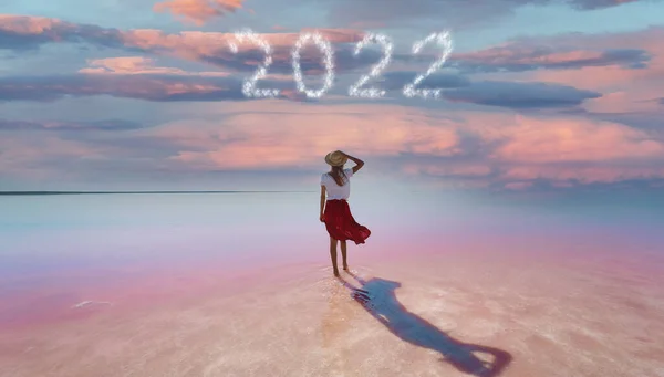 Woman traveler standing in beautiful pink lake with evening purple violet sunset sky with happy new year 2022 numbers — ストック写真