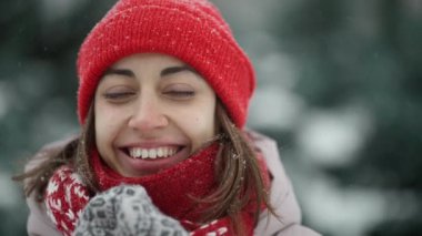 Karlı kış parkında kar taneleriyle dolu bir günde örgü örülü şapka ve eşarplı komik bir kadının 4 yavaş çekim portresi. Kadın buhar üflüyor, kendini atkıya sarıyor. Kış tatilin kutlu olsun, iyi eğlenceler..