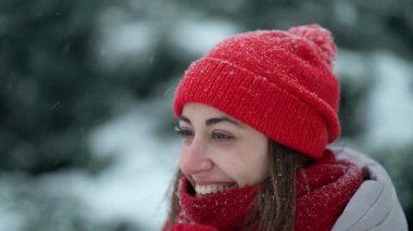 Kış parkında kar taneleriyle dolu bir günde örgü şapkalı ve eşarplı mutlu bir kadın. Kadın buhar üflüyor, yüzünde kar taneleri var. Kış tatilin kutlu olsun, iyi eğlenceler..