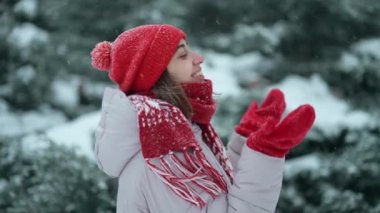 4K yavaş çekim kamerası, kırmızı eldivenli ve parka giymiş, karda karla eğlenen gülümseyen mutlu genç bir kadının etrafında dönüyor.