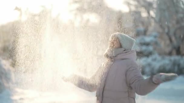 Sliw motion girl at winter time walks and haves fun outdoors. cheerful excited woman throws snow up and rejoices in flying snowflakes at sunny frosty winter day — Stock videók