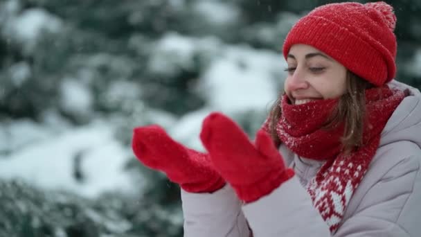 4k αργή κίνηση νέα όμορφη χαμογελαστή ευτυχισμένη γυναίκα με κόκκινα γάντια και καπέλο φορώντας μπουφάν περπατώντας στο πάρκο στο χιόνι, ζεστά ρούχα, διασκεδάζοντας — Αρχείο Βίντεο