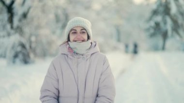 4K yavaş çekim neşeli güzel kadın kar yağdıktan sonra kış parkında yürüyor. Güneşli kış gününde ağaçlar karlar içinde. Mutlu heyecanlı kız dondurucu tazeliğin tadını çıkarıyor..