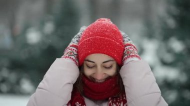 4k slow motion extreme close up face of beautiful smiling woman in knitted red beanie and scarf walking in park at winter outdoors. snowflakes blowing, woman cheerfuly smiles