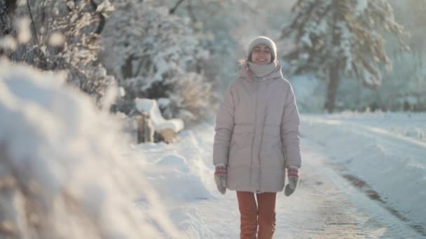 Радісна красива жінка, що йде на відкритому повітрі в морозному парку після снігопадів. зимовий час прогулянки і розваги на відкритому повітрі — стокове відео