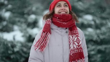 4k slow motion camera tracking shot of happy pretty woman in red mittens and hat walks in fir woods in snowy day, having fun with snow at winter holiday