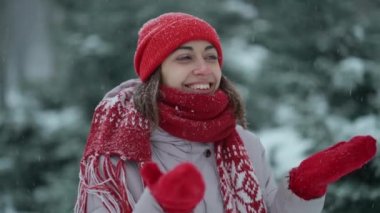 4K yavaş çekim kamerası, kırmızı eldivenli ve parka giymiş, karda karla eğlenen gülümseyen mutlu genç bir kadının etrafında dönüyor.