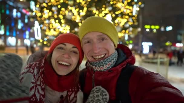 Pasangan bahagia memanggil kerabat mereka melalui video link pada tahun baru malam untuk suara lonceng di tengah jalan di lampu pasar Natal dengan latar belakang — Stok Video