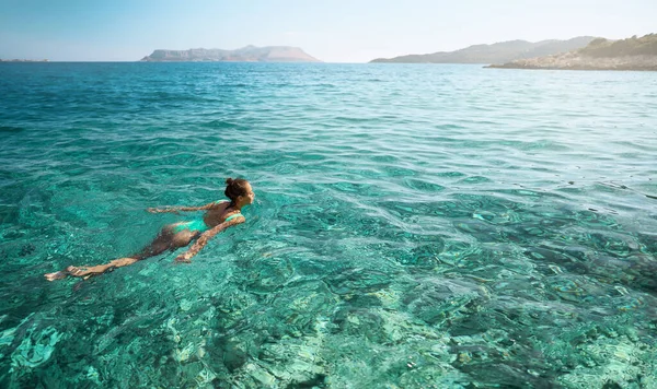 Nuori nainen ui kirkkaassa turkoosissa merivedessä ja katselee paratiisimaisemaa. — kuvapankkivalokuva