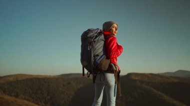 Sırt çantalı bir kadın gezgin kayalık bir tepede duruyor ve güneşli bir sonbahar günbatımında dağ manzarasına bakıyor..