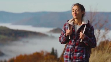 Neşeli hipster macerası genç kadın sabahın erken saatlerinde dağ geçidinde yürüyor, etrafa bakıyor, güzel manzaranın tadını çıkarıyor, mutlu hissediyor ve gün doğumunu selamlıyor, el kaldırıyor..