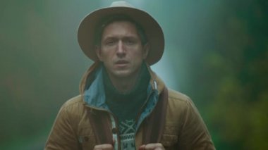 İnsan otostopçunun eski tarz giydiği yumuşak odak portresi. Sırt çantalı gezgin soğuk ve nemli bir sonbahar gününde dışarıda duruyor ve bir araba bekliyor. Adam doğrudan kameraya bakıyor.