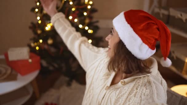 POV eerste persoon bekijk gelukkig vrolijk opgewonden vrouw in feestelijke Santa Hat het nemen van selfie op de achtergrond van versierd huis met kerstboom — Stockvideo