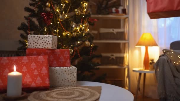 O b-rolo de mãos de mulheres põe o vermelho festivo na mesa abaixo da árvore de Natal de decorador no quarto à noite. iluminação guirlanda e vela ardente irradiando espíritos de Natal e humor — Vídeo de Stock