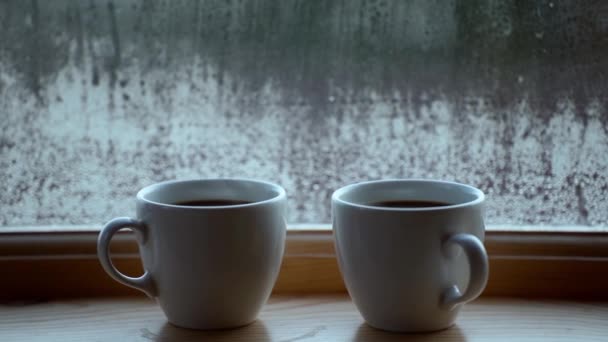 Dos tazas de café de bebida caliente cerca de la ventana, condensación de agua en el vidrio de la ventana, temprano en la mañana, despertar concepto — Vídeo de stock
