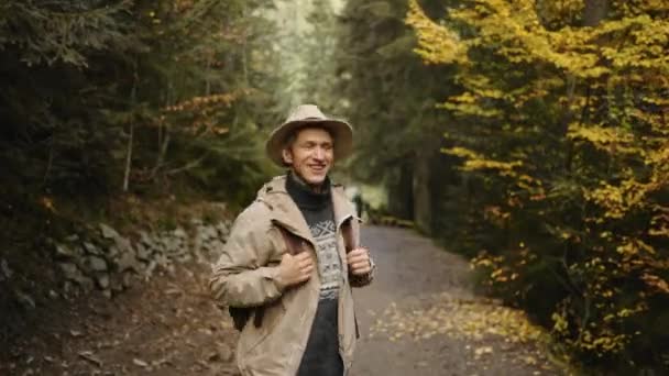 Gelukkige hippe man in casual kleding en hoed Wandelen in het bos in de herfst. Actieve gezonde blanke man met een rugzak nemen in hout. mannelijke reiziger wandelingen langs bos, recreatie, bio-toerisme, Wandelen — Stockvideo