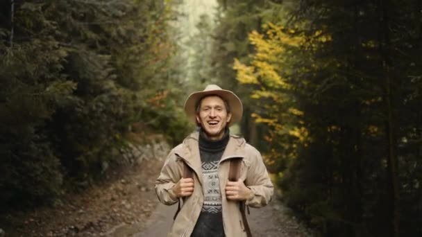 Улыбающийся турист средних лет в повседневной одежде и шляпе Пешие прогулки в лесу осенью. Активный здоровый белый мужчина с рюкзаком, гуляющий по лесу. мужчины прогулки в лесу, досуг, био-туризм — стоковое видео