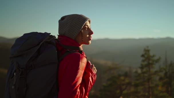 Πλάγια πορτρέτο γυναίκα πεζοπόρος με σακίδιο στέκεται στο φως ηλιοβασίλεμα μεταξύ των βουνών και λόφων, κλείστε επάνω αργή κίνηση. επιτυχής ανάβαση στην κορυφή του βουνού — Αρχείο Βίντεο