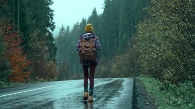 Sırt çantalı otostopçu kadın soğuk ve nemli bir sonbahar gününde alog yolunda yürüyor ve bir araba bekliyor. Otostop çekerek dağ doğası tatil seyahat turizm özgürlüğü