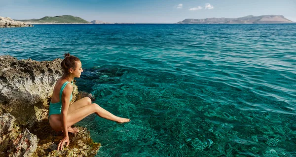 Hermosa chica sexy modelo sentado en el acantilado por el agua de mar turquesa, destino de playa tropical — Foto de Stock