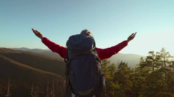 Портрет повільної безтурботної дівчини з рюкзаком розслабляє і насолоджується видом на захід, піднімаючи руки на красивому ландшафті в горах, стоячи на тлі блакитного неба на заході сонця. вибірковий фокус — стокове відео