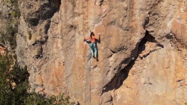 Luftaufnahme von der Drohne eines kräftigen, muskulösen jungen Mannes, der am Seil hängt und nach dem Klettern auf einem hohen Felsen durch eine herausfordernde Kletterroute abstürzt. — Stockvideo