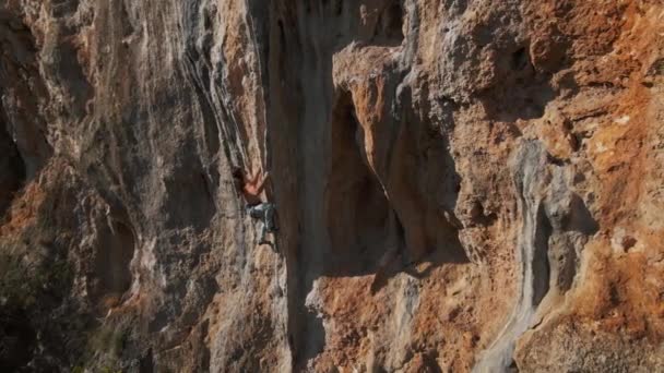 Imágenes de drones aéreos en cámara lenta de un hombre fuerte escalador escalando en una dura ruta dura en un risco vertical con una enorme toba. escalador hace varios esfuerzos difíciles y movimientos para aferrarse — Vídeos de Stock