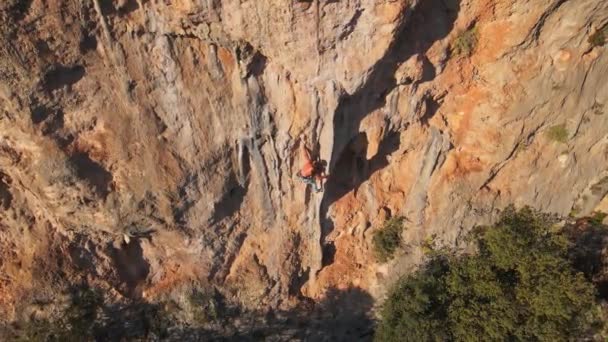 Luftaufnahme von der Drohne eines kräftigen, muskulösen jungen Mannes, der am Seil hängt und nach dem Klettern auf einem hohen Felsen durch eine herausfordernde Kletterroute abstürzt. — Stockvideo