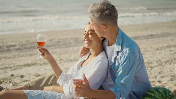 Portrettelskende par som omfavner, drikker vin og nyter piknik på stranden – stockfoto