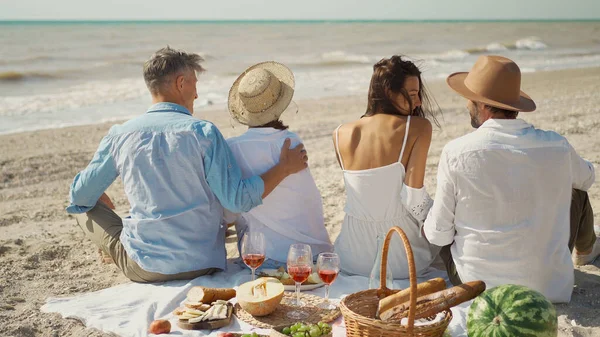 Takanäkymä pari ystäviä rannalla ottaa piknik juhla viiniä ja maukas ateria. — kuvapankkivalokuva