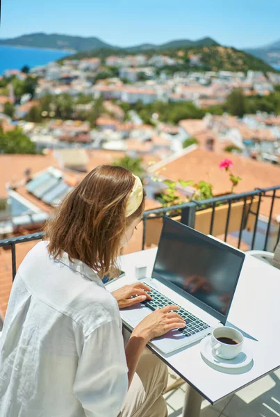 Taustakuva nainen käyttää kannettavaa tietokonetta työskentelee kirjoittamalla verkossa yli Välimeren näkymä ulkopuolelta parveke — kuvapankkivalokuva