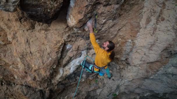 Von oben filmische Zeitlupe eines starken, geschickten Bergsteigers, der auf überhängende Felswände klettert. Mann macht schwierige und zähe Anstrengungen und Bewegungen. — Stockvideo