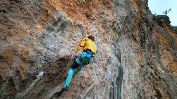 Zeitlupe eines fröhlichen, gut aussehenden Bergsteigers in gelbem Sweatshirt mit langen Haaren, die am Seil hängen und nach erfolgreicher Besteigung der Route auf einer Klippe hoch fünf geben. — Stockvideo