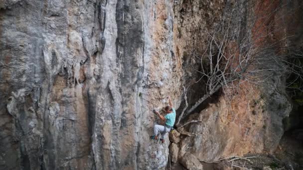 Вид зверху дорослий чоловік скелелазний сходження вгору по високій скелі, що робить важкий хід вгору, досягаючи і захоплюючи мотузку — стокове відео