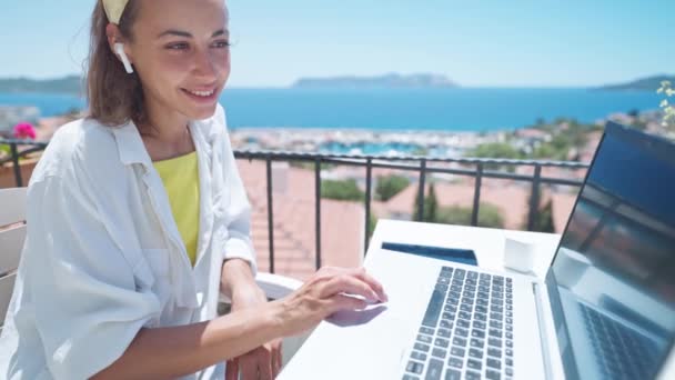Seitenporträt Freiberuflerin mit Laptop beim Surfen im Internet Nachrichten checken, in drahtlosen Kopfhörern genießen die Arbeit auf der Terrasse im Freien Café — Stockvideo
