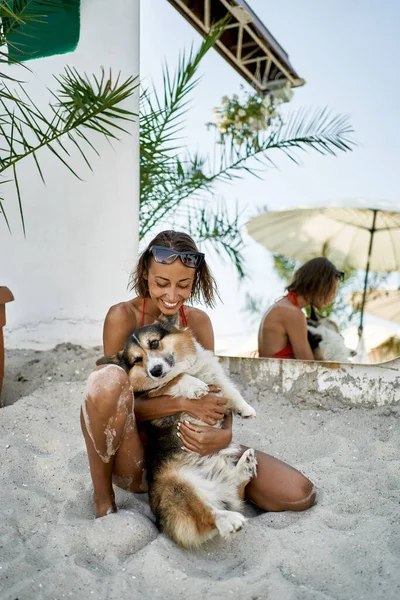 Счастливая девушка обнимает свою смешную собаку на пляже у своей виллы — стоковое фото