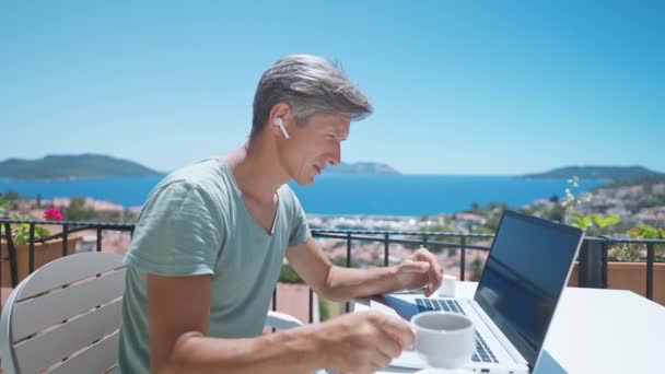 Side view średnim wieku kaukaski mężczyzna biznes trener dając wywiad online przemawiając na laptopie kamery o odległe spotkanie z szefem poza biurem w kawiarni w lecie morze podróże — Wideo stockowe