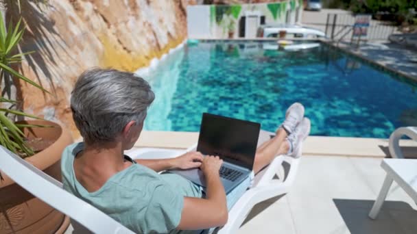 Вид збоку розслабляючий дорослий чоловік охолоджує біля басейну під час відпустки в курортному готелі, переглядаючи новини або відео на ноутбуці порожній екран — стокове відео
