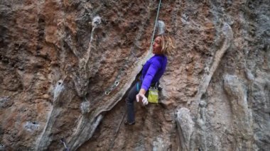 Ağır çekimde gülümseyen yorgun ama mutlu kadın kaya tırmanışçısı uçurumun tepesinde zorlu bir yolda asılı duruyor. Komik kız dinleniyor, eğleniyor, surat asıyor ve nasıl tırmanacağını araştırıyor..