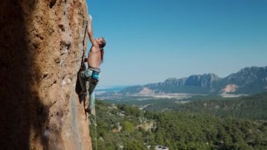 Zinde bir adam dağa tırmanıp bir sonraki hamlesine odaklanarak kaya tutucularına ulaşır. Sinematik yavaş çekim, fitness