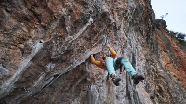 慢动作微笑疲惫的攀岩者挂在悬崖峭壁上的硬挑战路线上。男人躺着，用粉笔画着双手，看怎样爬得更远. — 图库视频影像