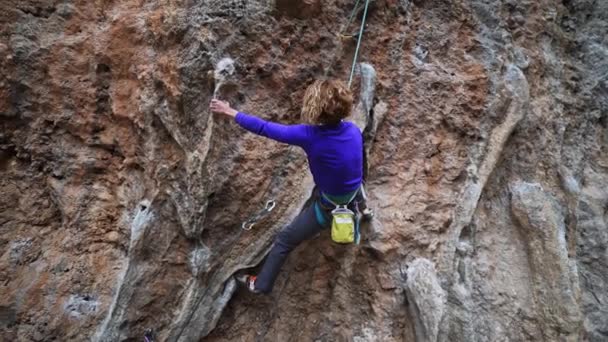 Slow motion smiling tired woman rock climber hanging on rope on hard challenge route on overhanging cliff, resting and chalking hands — Stock Video