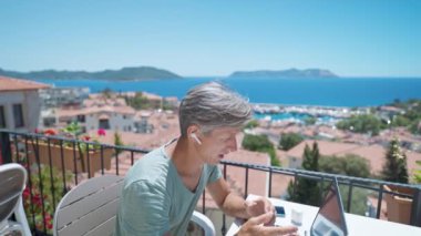 Yan görünüm: Orta yaşlı beyaz adam iş koçu internet röportajı yapıyor ya da webcam laptop 'da danışmanlık yapıyor yaz deniz seyahatlerinde ofisin dışındaki kafede ekiple uzak bir toplantı yapıyor.