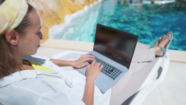 Câmera zoom fora da mulher desfrutando de relaxar na piscina com computador portátil com tela vazia, digitação, navegação, ordem on-line durante as férias no hotel resort — Vídeo de Stock