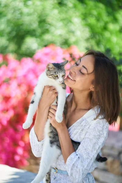 Spring portrait charming woman holding cat at garden with pink flowers — Stock Photo, Image