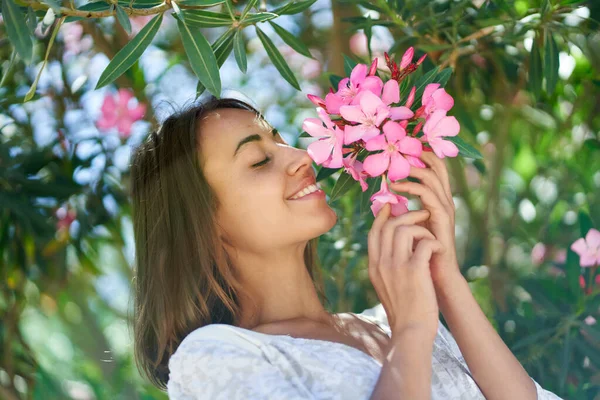 Vakker, lystig kvinne som tar på rosa blomster og nyter lukten i hagen. – stockfoto